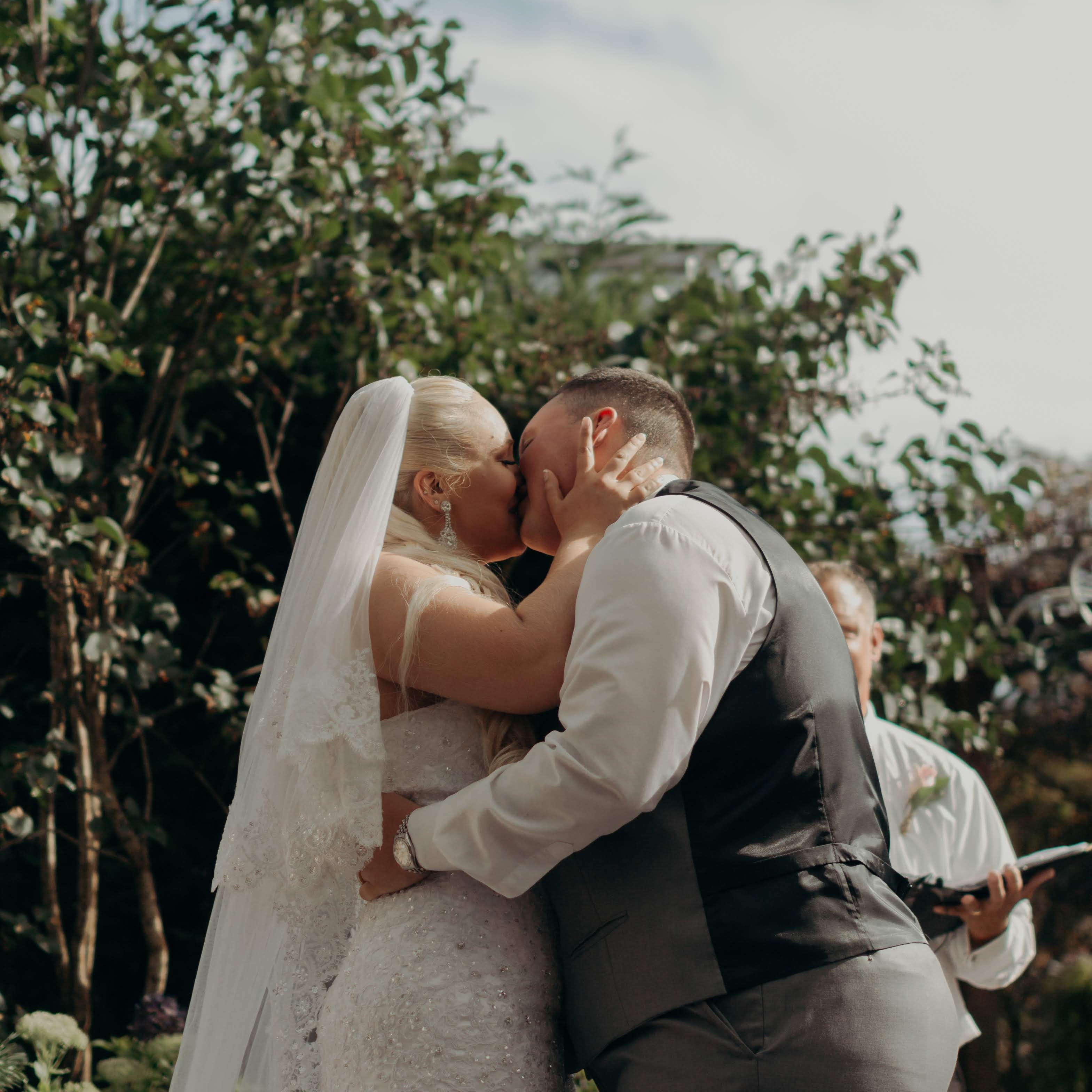 Couple kissing outdoors with trees and clear sky in the background